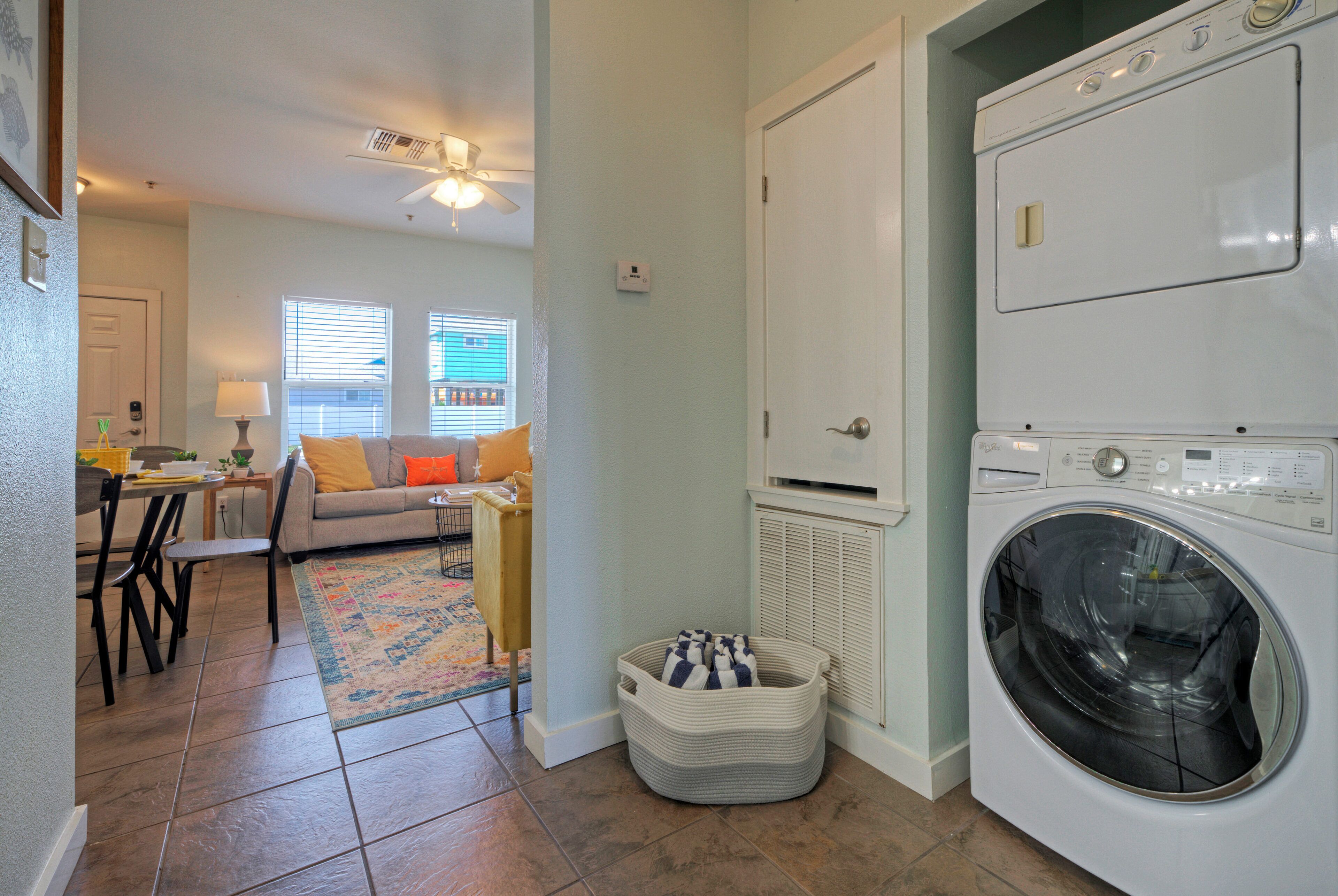 A laundry room with a front-loading washing machine, a small seating area with a sofa and a chair, and a rug on the floor.