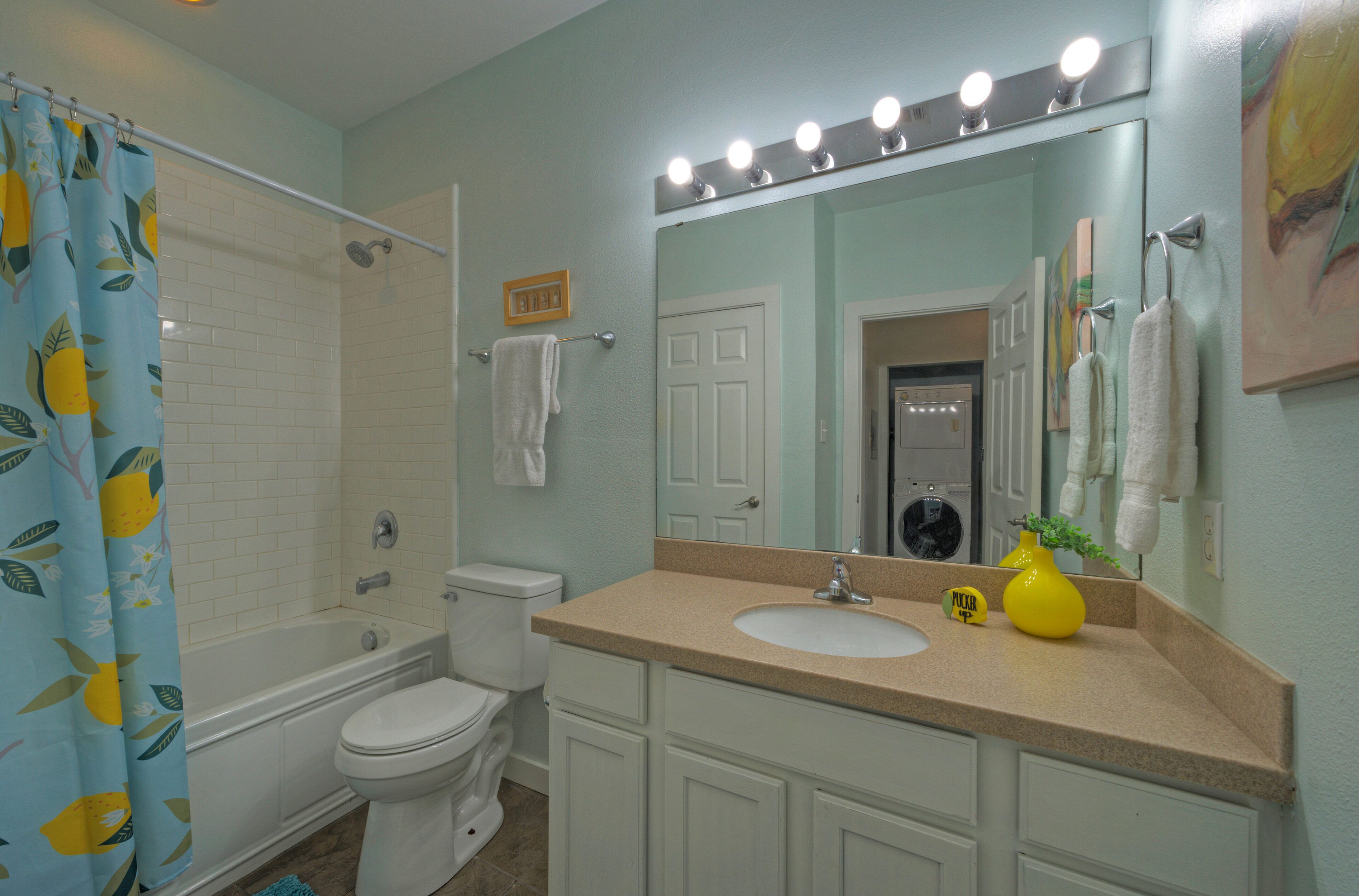 A bathroom with a bathtub, toilet, sink, and a mirror with lights.