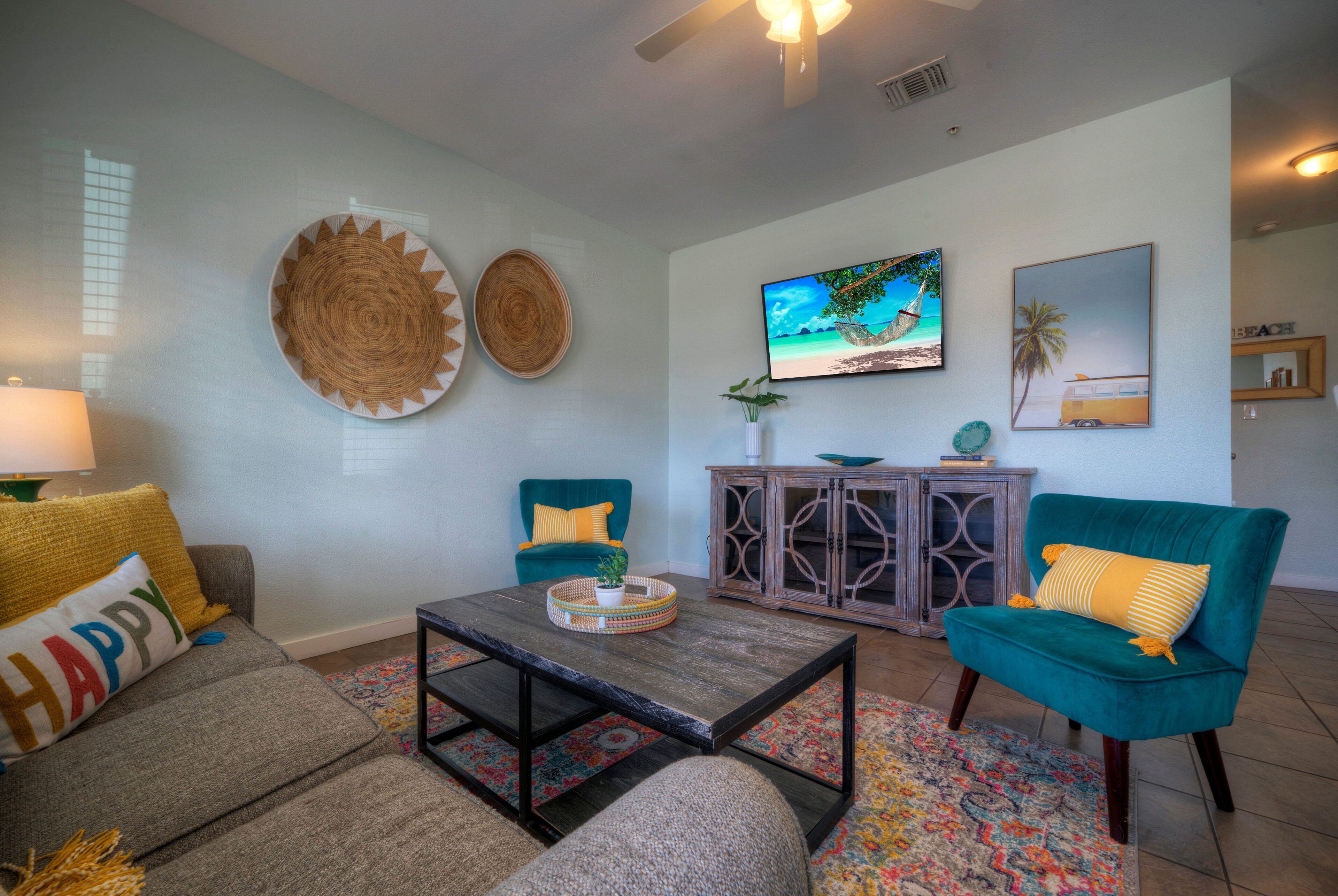 A living room with a sofa, armchair, coffee table, and a TV on the wall.