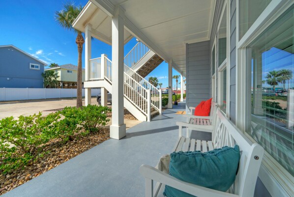 A covered porch with white benches and a staircase leading to a second floor.