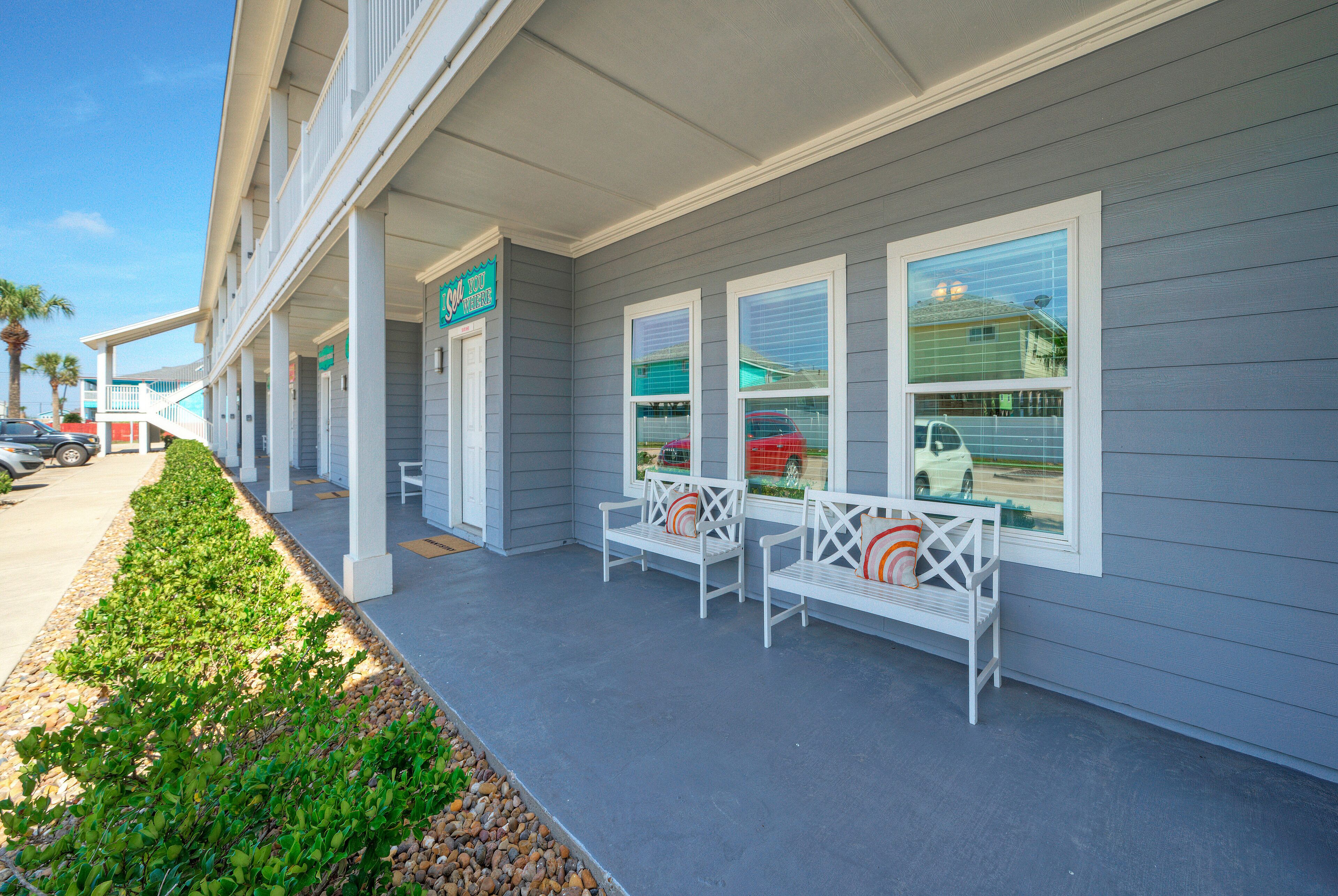 A building with a covered porch, white benches, and a green sign.