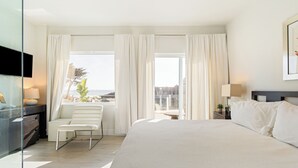 A hotel room with a large bed, a seating area with a chair and a table, a TV, and a view of the outdoors. - 7 Bungalows | Steps to Pier + Beach | Ocean Views, Outdoor Bar, Firepit, Lounge (Cayucos)