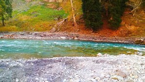 A river with clear water, surrounded by rocky terrain and trees. - Hotel Neel Gagan (Gund)