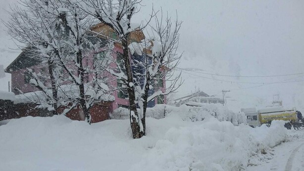 A snowy residential area with a house partially covered in snow, a road, and a snowplow. - Hotel Neel Gagan (Gund)