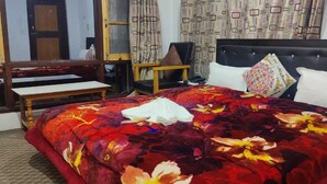 A hotel room with a large bed, a wooden bench, a chair, and a small table. - Hotel Neel Gagan (Gund)