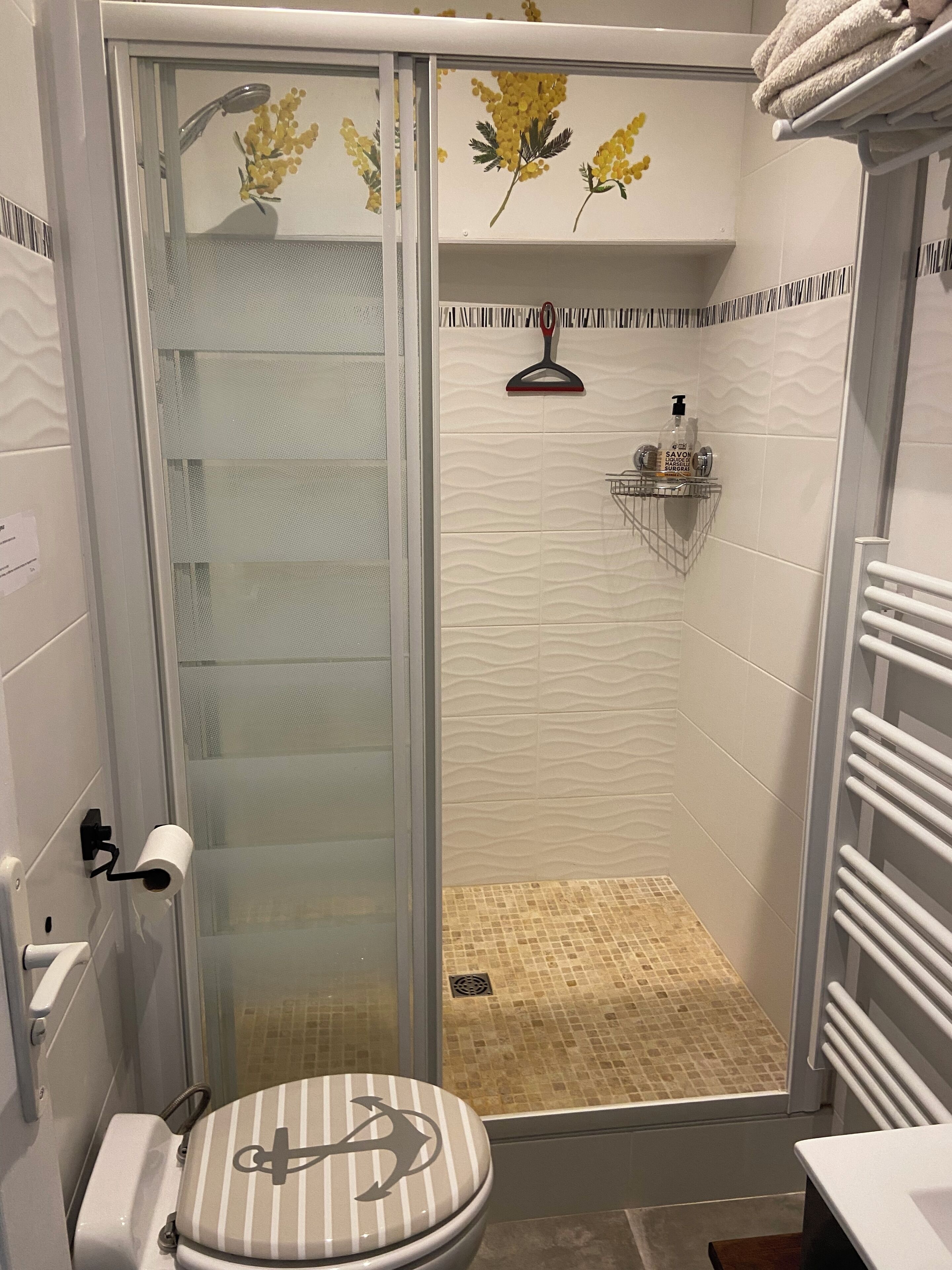 A shower with a glass door, a toilet with a striped seat, and a towel rack with towels.
