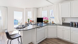 Una cocina moderna con armarios blancos, encimera negra y vistas a la ciudad a través de amplios ventanales.