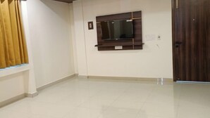 A room with a large window, a mounted flat-screen TV, and a wooden door. - Hotel Ganga Greens (Lucknow)