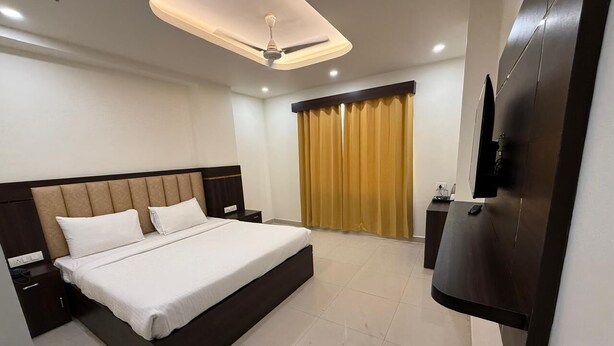 A modern hotel room with a large bed, a flat-screen TV mounted on the wall, and a ceiling fan. - Hotel Ganga Greens (Lucknow)