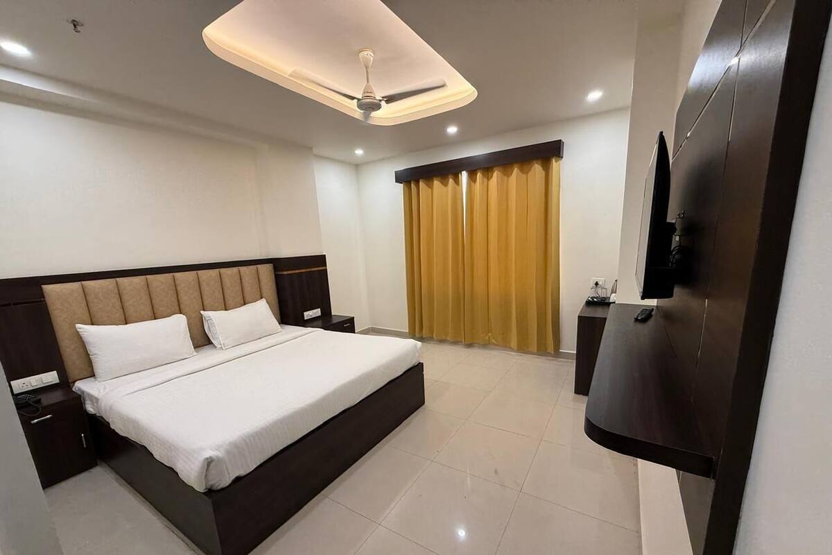A modern hotel room with a large bed, a flat-screen TV mounted on the wall, and a ceiling fan.