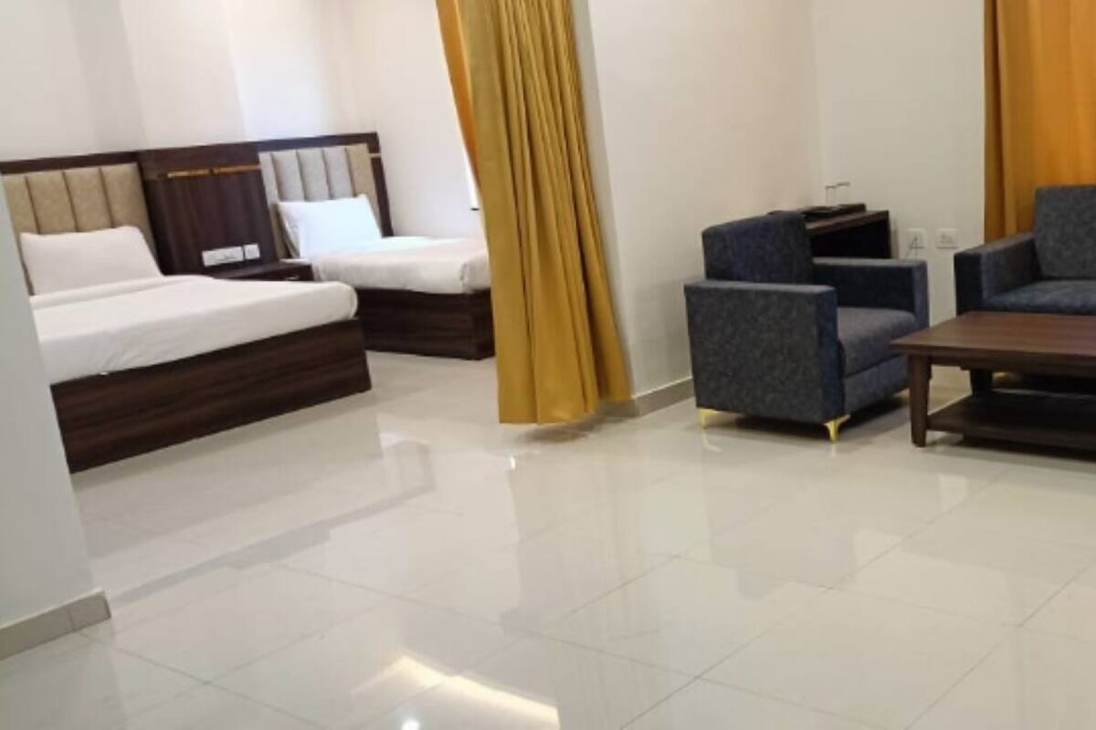 A modern hotel room with a bed, two armchairs, a sofa, a coffee table, and a TV.