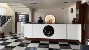 A hotel reception area with a checkered floor, a reception desk with a logo, and a staircase. - Hotel Ganga Greens (Lucknow)