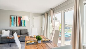 Un salón moderno con una mesa de comedor de madera, sillas blancas, un sofá gris y un cuadro abstracto colorido en la pared.