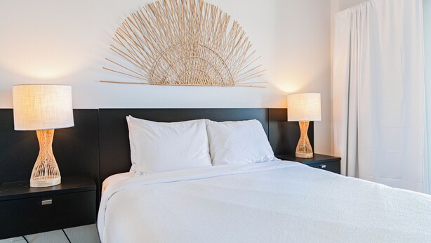 Una habitación de hotel con una cama grande, dos lámparas de noche, un adorno en la pared y una ventana con cortinas.