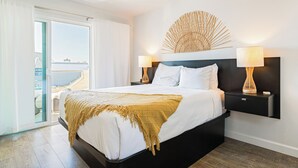 Ein modernes Hotelzimmer mit einem großen Bett, einem Nachttisch, einer Wandlampe und Meerblick durch eine Schiebetür.