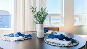 Ein runder Esstisch mit einer weißen Vase, gefüllt mit Grünpflanzen, blauen Servietten und weißen, rechteckigen Gegenständen auf gewebten Tischsets.