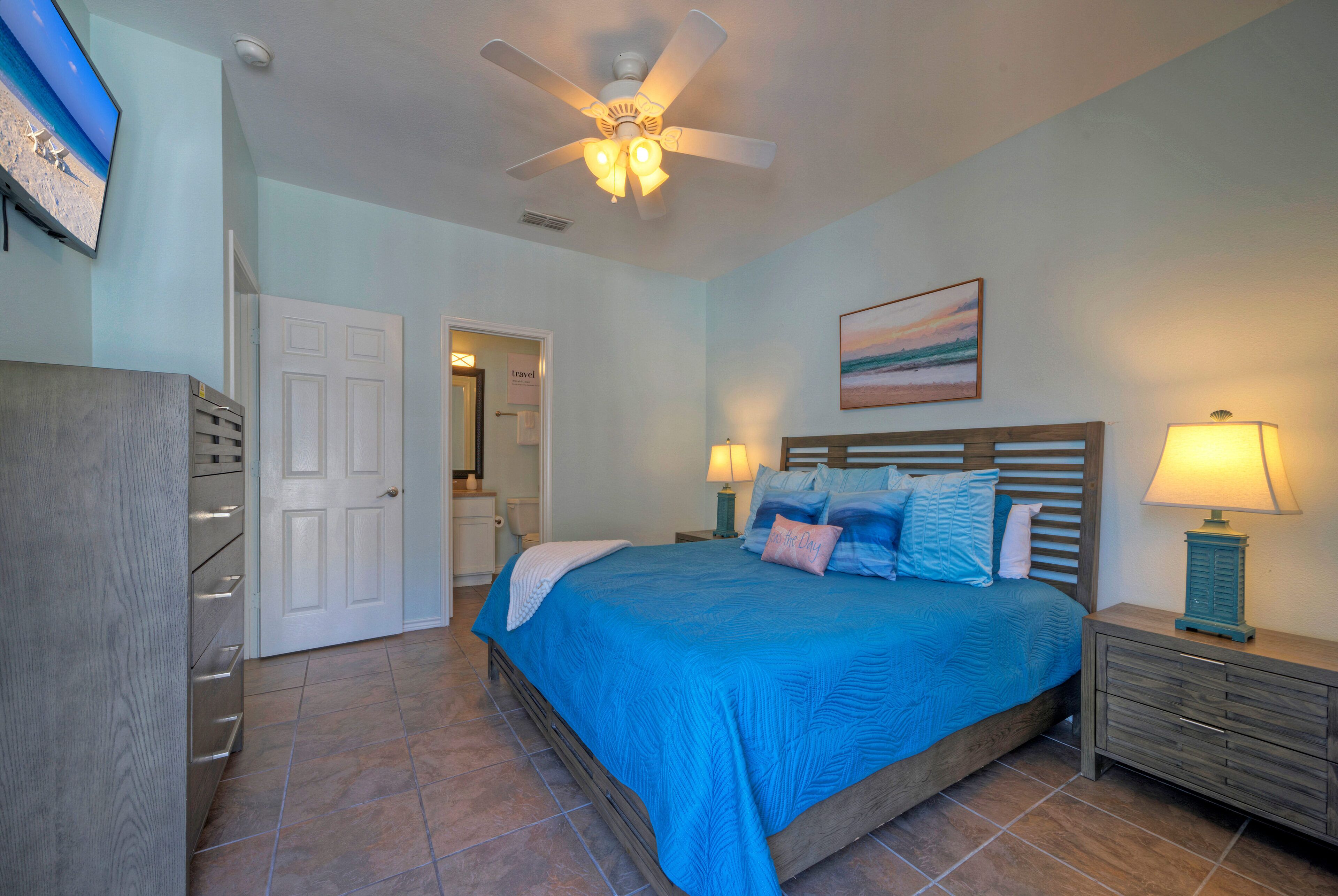 A bedroom with a bed, nightstands, a ceiling fan, a TV, and a door.