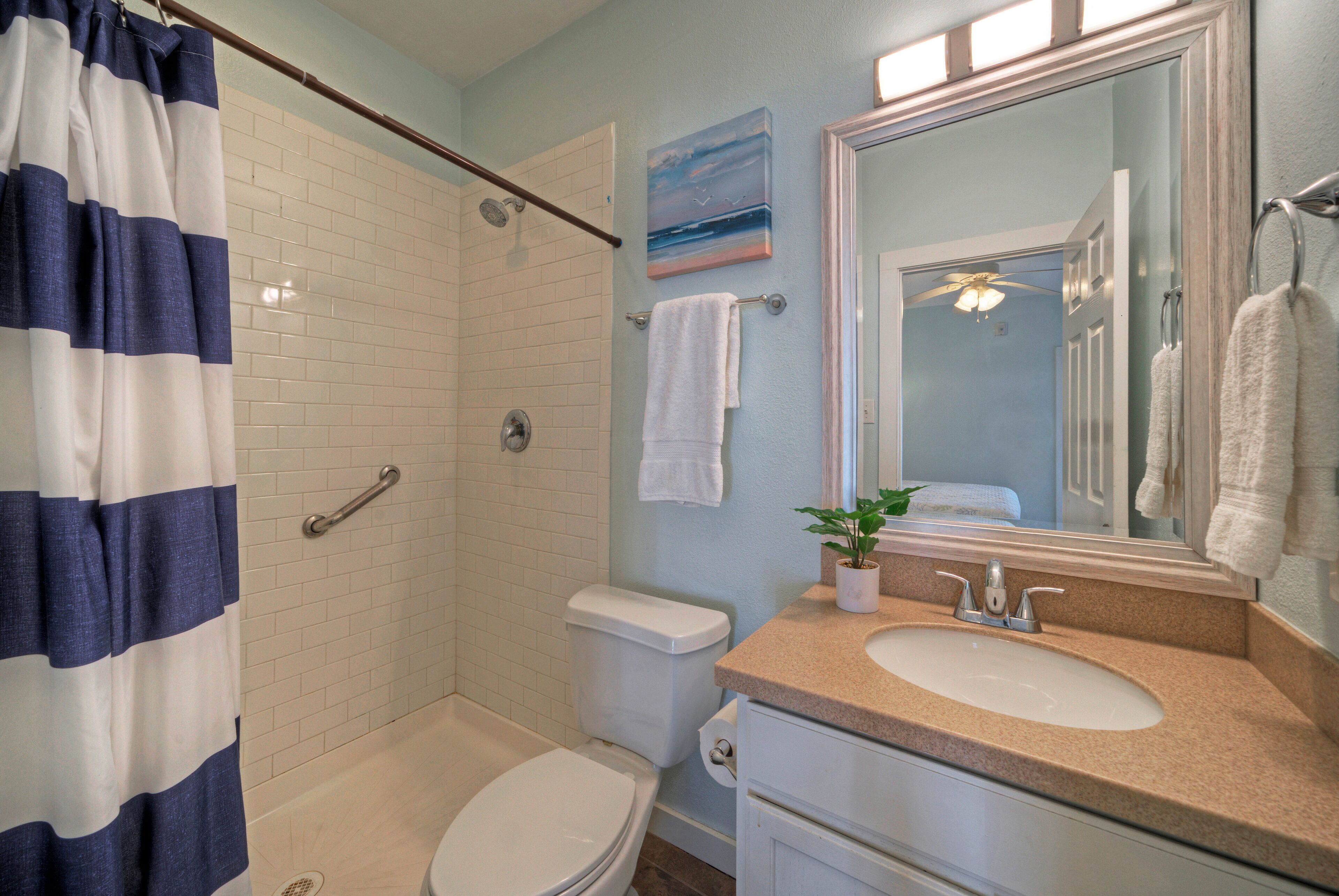 A bathroom with a shower, toilet, sink, and a large mirror.