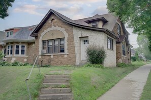 Une maison à deux étages avec une façade en pierre, un porche à l’avant et un escalier apparent menant à l’entrée.