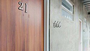 A wooden door with the number 21, a metal handle, and a concrete wall with a window and a door to the right. - Rumah Betawi Kalipasir (Jakarta)