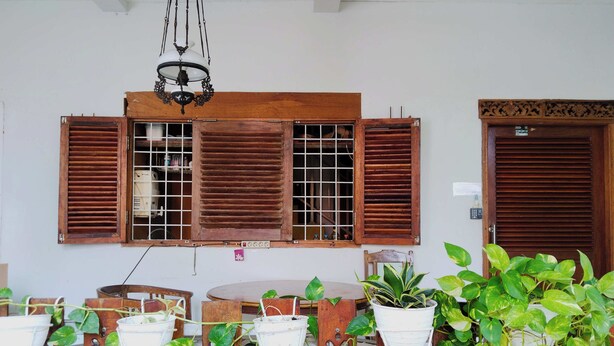 A room with wooden furniture, a large window with shutters, and potted plants. - Rumah Betawi Kalipasir (Jakarta)