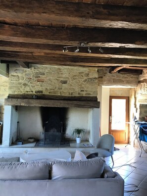 A rustic interior with a stone fireplace, wooden beams, a sofa, and a door leading outside.