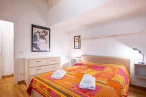Un dormitorio con cama, mesita de noche, cómoda, cuadro enmarcado y estante.