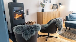 A cozy living room with a wood-burning stove, a blue sofa, and a chair with a fur throw.