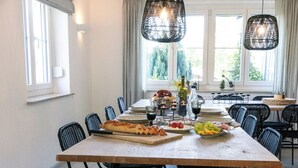 A dining area with a long table, black chairs, and hanging black pendant lights.