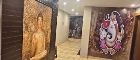 Ein Flur mit Buddha-Statue und Ganesha-Wandgemälde, der zu einem Raum mit Fliesenboden führt.
