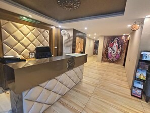 Een receptiegebied van een hotel, modern ingericht, met een receptiebalie, een zithoek en een muur met een muurschildering.