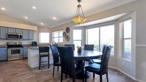 A modern kitchen with stainless steel appliances, a dining area with a round table and chairs, and large windows providing natural light.