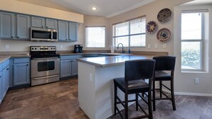 A modern kitchen with stainless steel appliances, a central island, and a dining area with two chairs.
