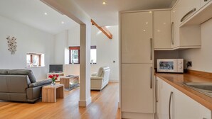 A modern living room with a sofa, a coffee table, and a TV. There is a kitchen area with cabinets and a microwave. - Cottage in St Breward near Bodmin Moor (St Breward)