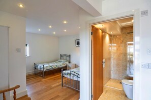 A bedroom with two single beds, a wooden floor, and a bathroom with a shower and toilet. - Cottage in St Breward near Bodmin Moor (St Breward)
