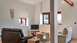 A modern living room with a sofa, a recliner, a TV, and a small table with a vase of flowers. - Cottage in St Breward near Bodmin Moor (St Breward)