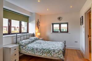 A bedroom with a bed, bedside table, lamp, window, and a heart-shaped decoration on the wall. - Cottage in St Breward near Bodmin Moor (St Breward)