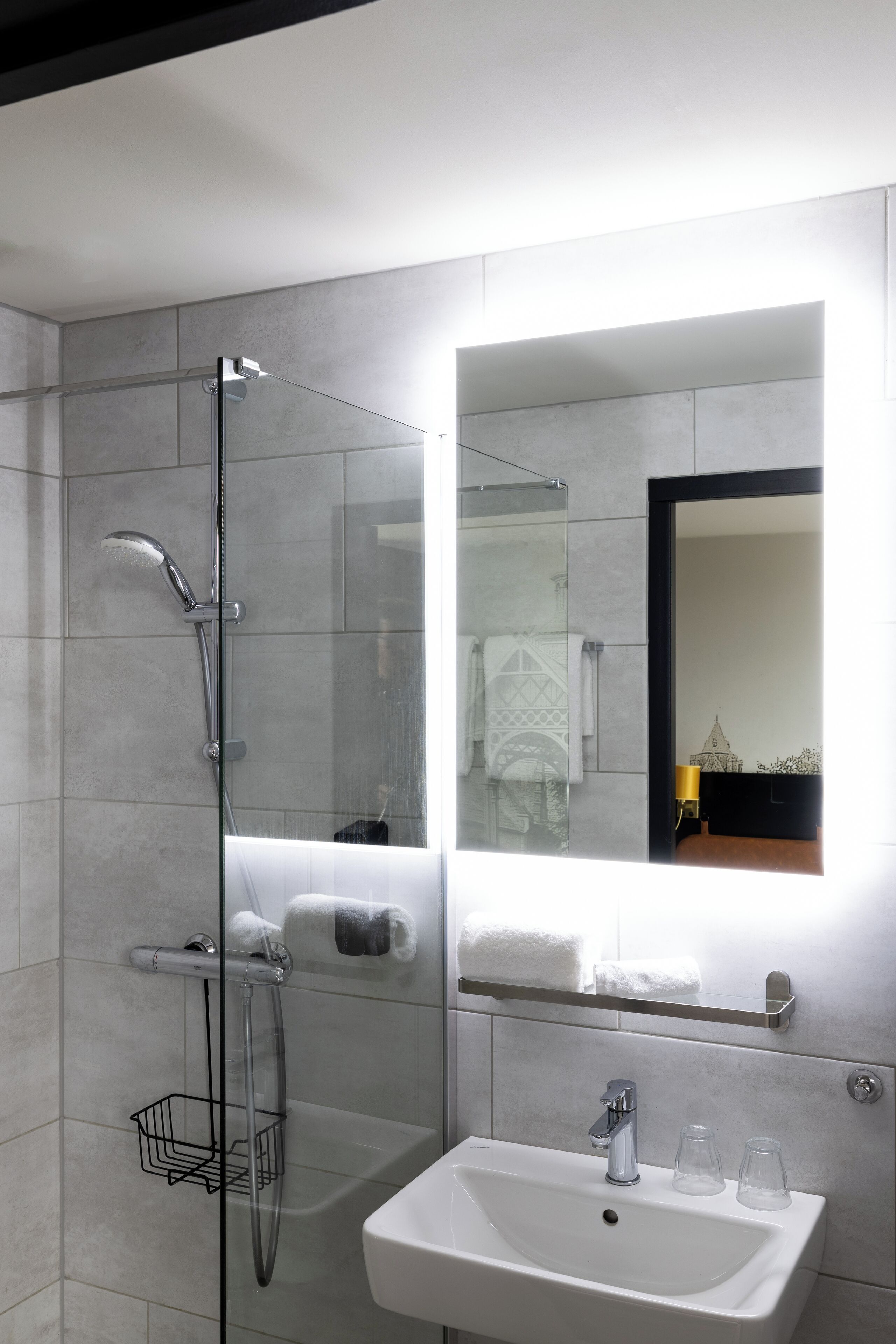 Un baño moderno con ducha de vidrio, un lavamanos blanco y un espejo sobre el lavamanos.