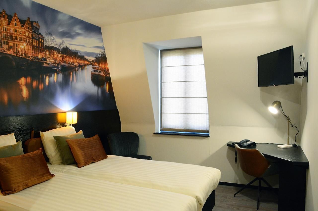 Habitación de hotel con una cama grande, un escritorio con silla, televisor montado en la pared y ventana con persianas.