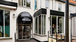 A white building with a red-tiled roof, a black awning, and a glass door entrance. - Boutique Hotel de Statie (Valkenswaard)