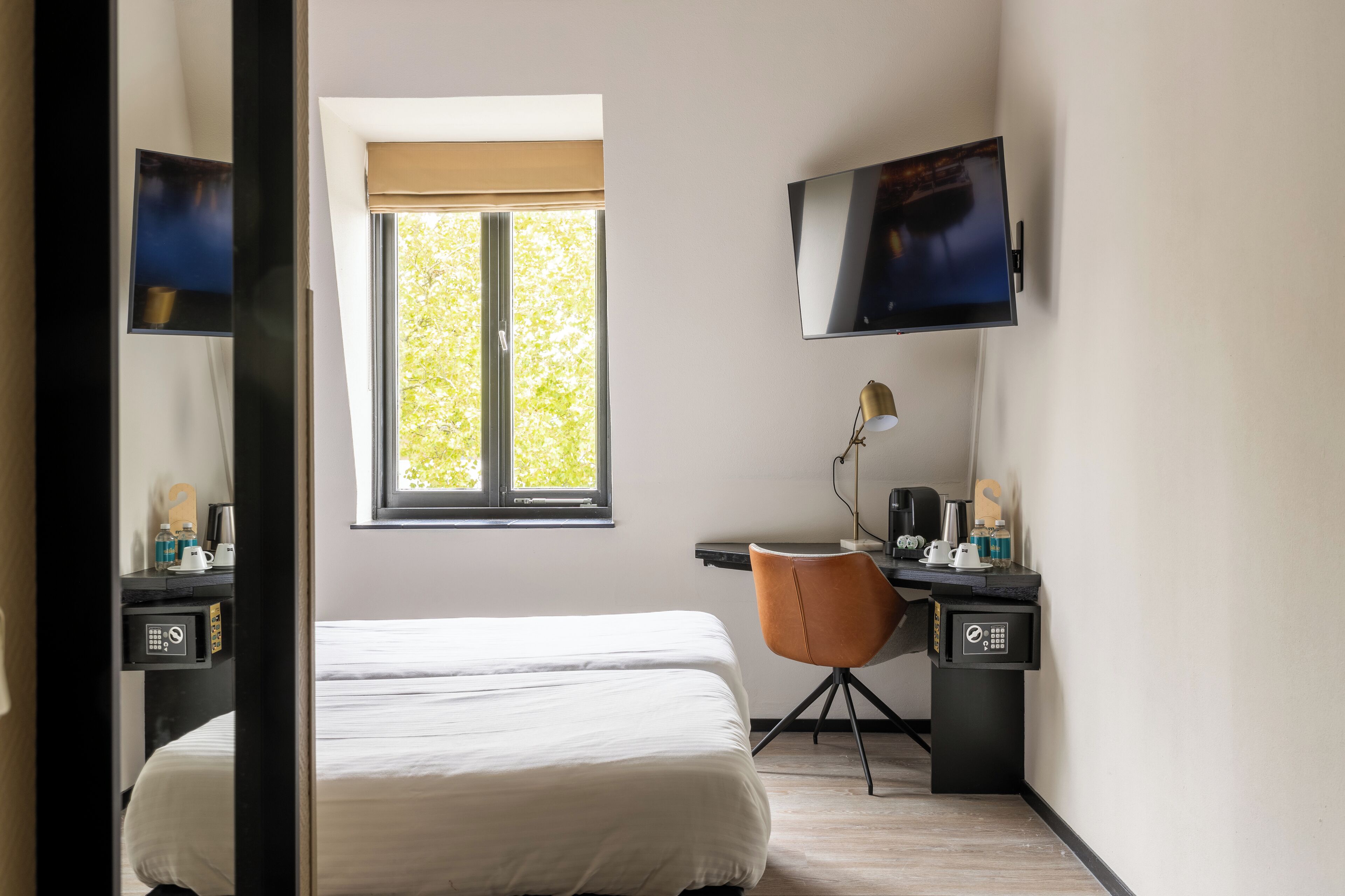 Una habitación de hotel con cama, escritorio, silla, televisor y ventana.