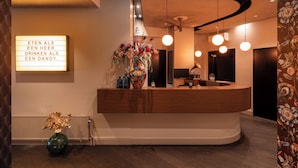 A reception area with a wooden counter, a floral arrangement, and a sign with text. - Boutique Hotel de Statie (Valkenswaard)