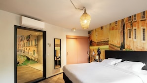 A hotel room with a bed, a mirror, a door with a view of a canal, and a wall with a mural. - Boutique Hotel de Statie (Valkenswaard)