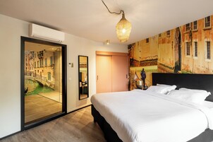 A hotel room with a bed, a mirror, a door with a view of a canal, and a wall with a mural.