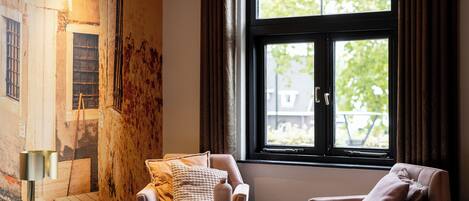 A hotel room with a bed, two armchairs, a small round table, and a large window with curtains.