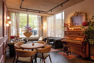 A cozy living room with a piano, leather sofas, a dining table, and a large window with curtains.