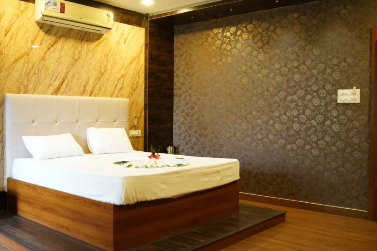 A neatly made bed with white linens and a decorative flower arrangement, a wooden headboard, and a patterned wallpaper wall.