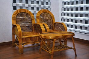 Una habitación con dos sillones de mimbre, una mesita y un suelo de madera. Se aprecia una ventana con diseño.
