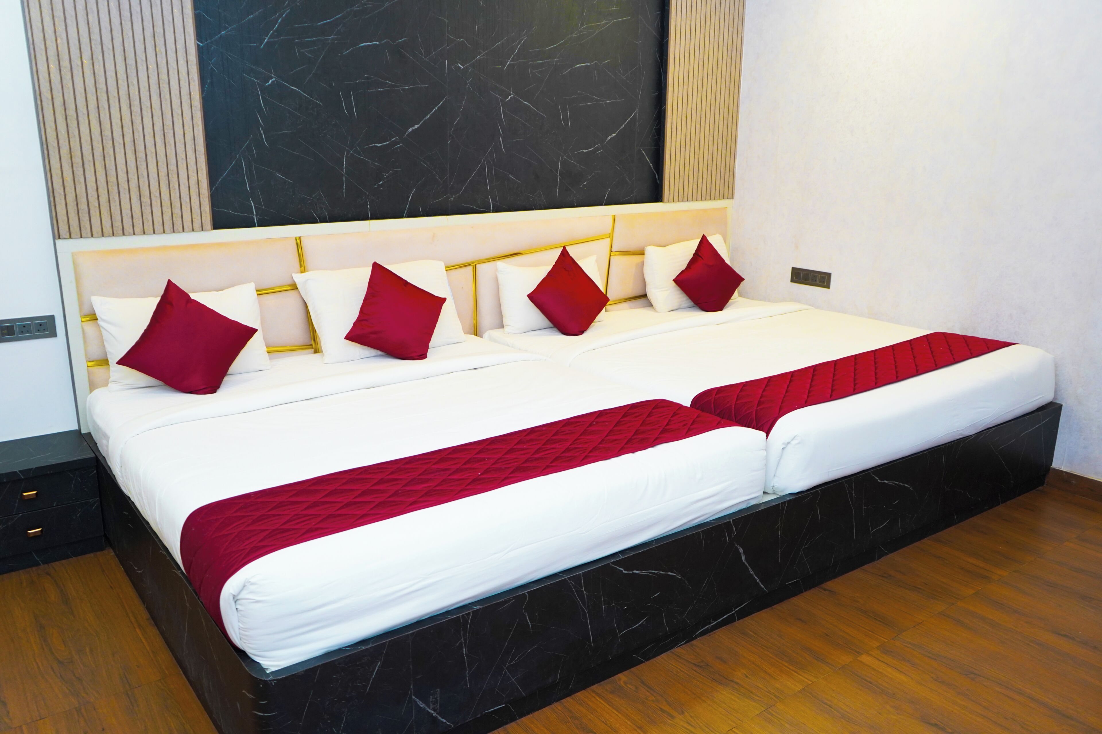 Ein Doppelbett mit weißer und roter Bettdecke, ein Kopfteil mit goldener Rahmung und eine Wand mit Marmoroptik dahinter.