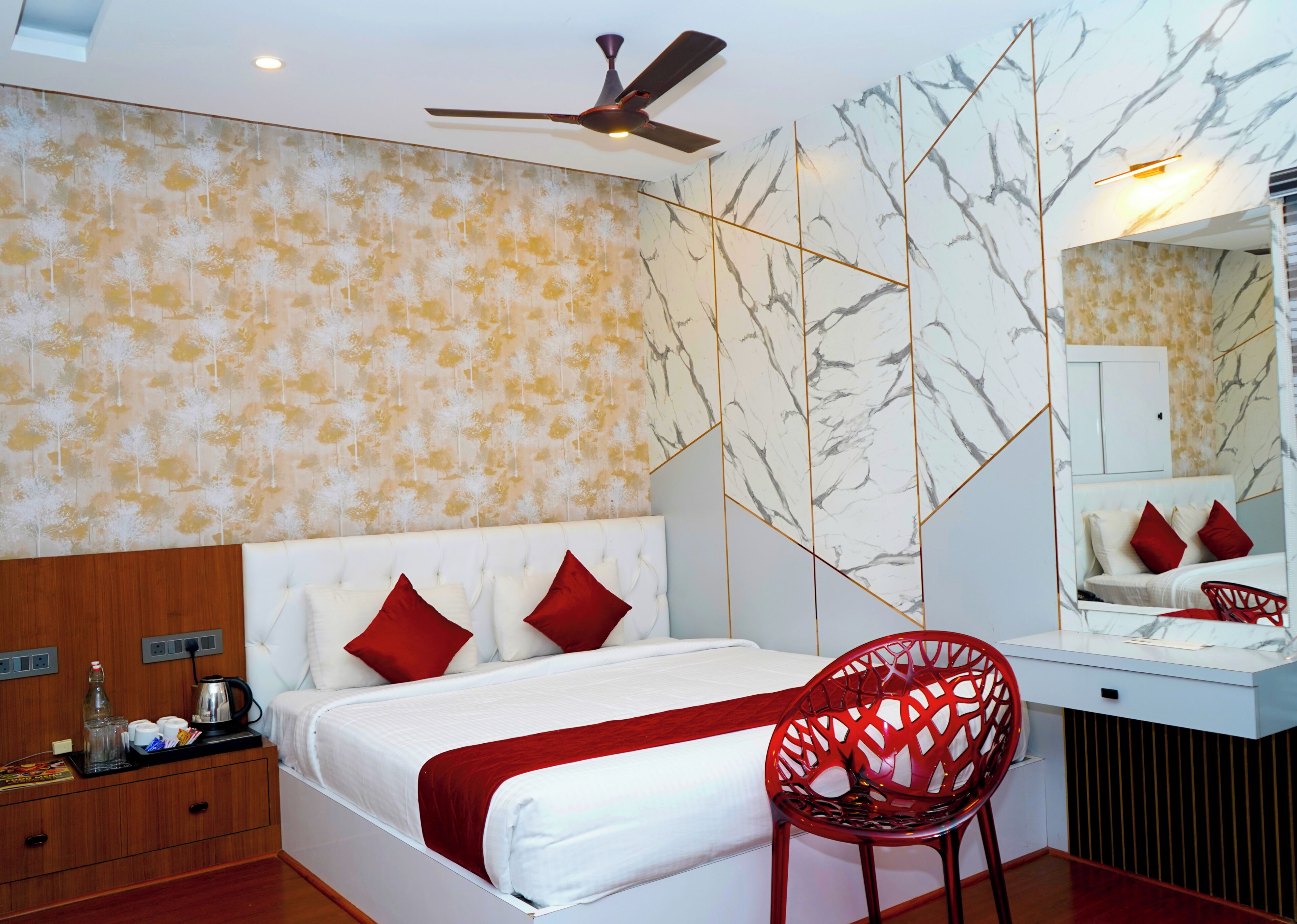 A hotel room with a bed, a red chair, a ceiling fan, and a wall with a leaf pattern.